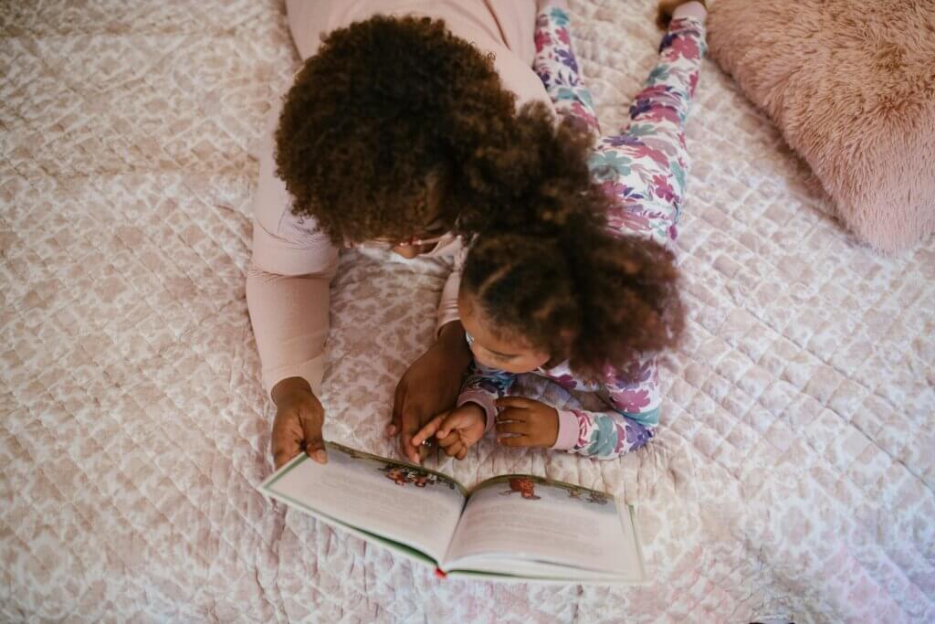 Mom and daughter laying in bed reading a book.