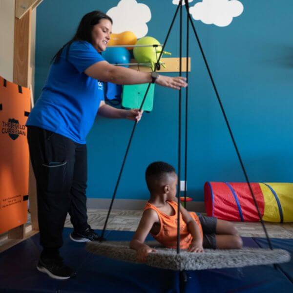 Child with autism working with a Hopebridge staff member on an occupational therapy swing.