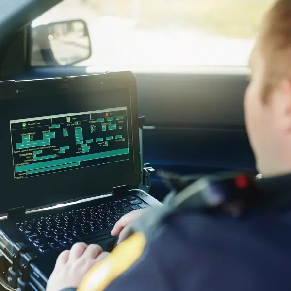 Over the shoulder perspective of officer in patrol car looking at computer.