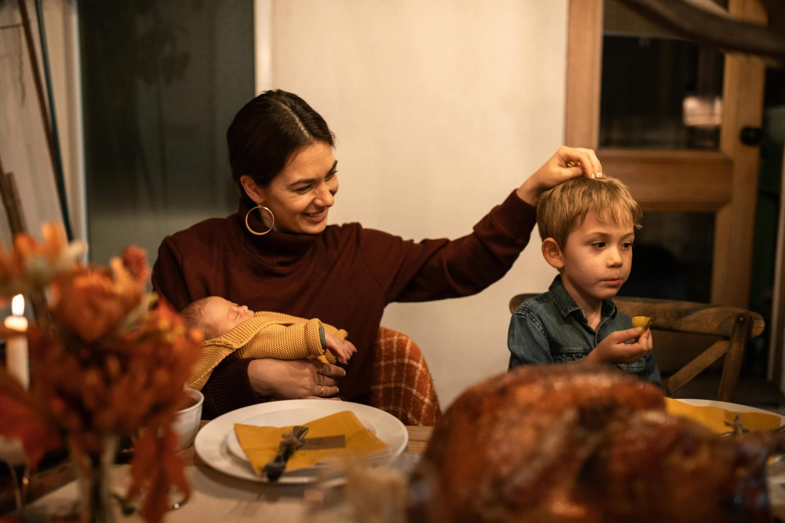 Mom, baby and young son sitting at the Thanksgiving table in front of food. Boy is a picky eater and eating only bread.