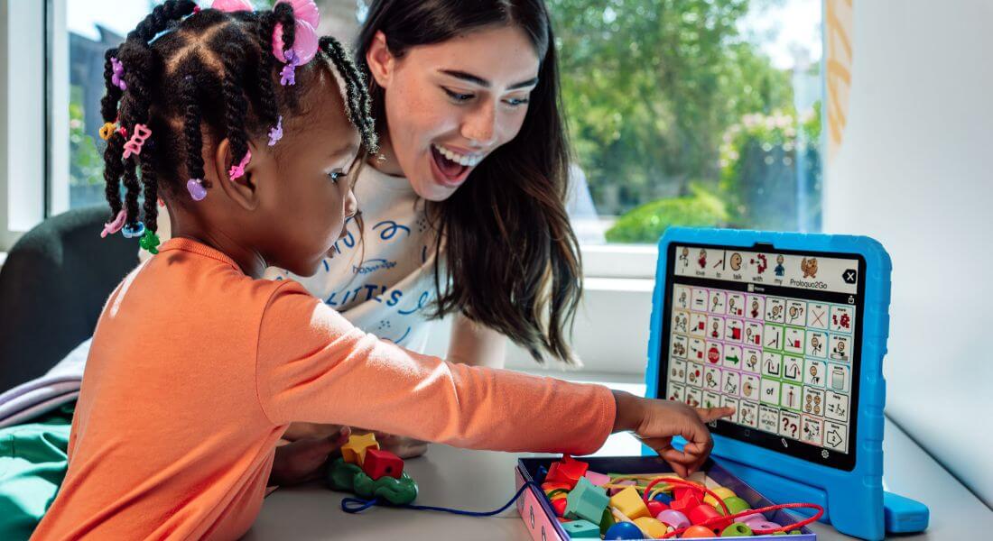 Photo of child and speech pathologist using an AAC device.